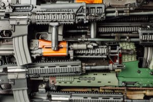 A close-up view of several modern rifles and firearms stacked together, showing various parts and details of the weapons.